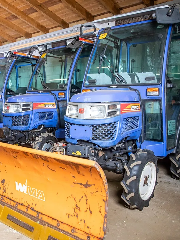 Traktor mit orangefarbenem Räumschild in einer Halle, dahinter weitere Traktoren