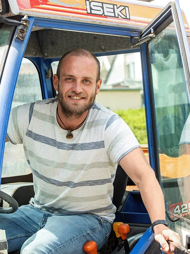 Falk Selz sitzt lächelnd am Steuer eines Traktors, die Kabinentür steht offen
